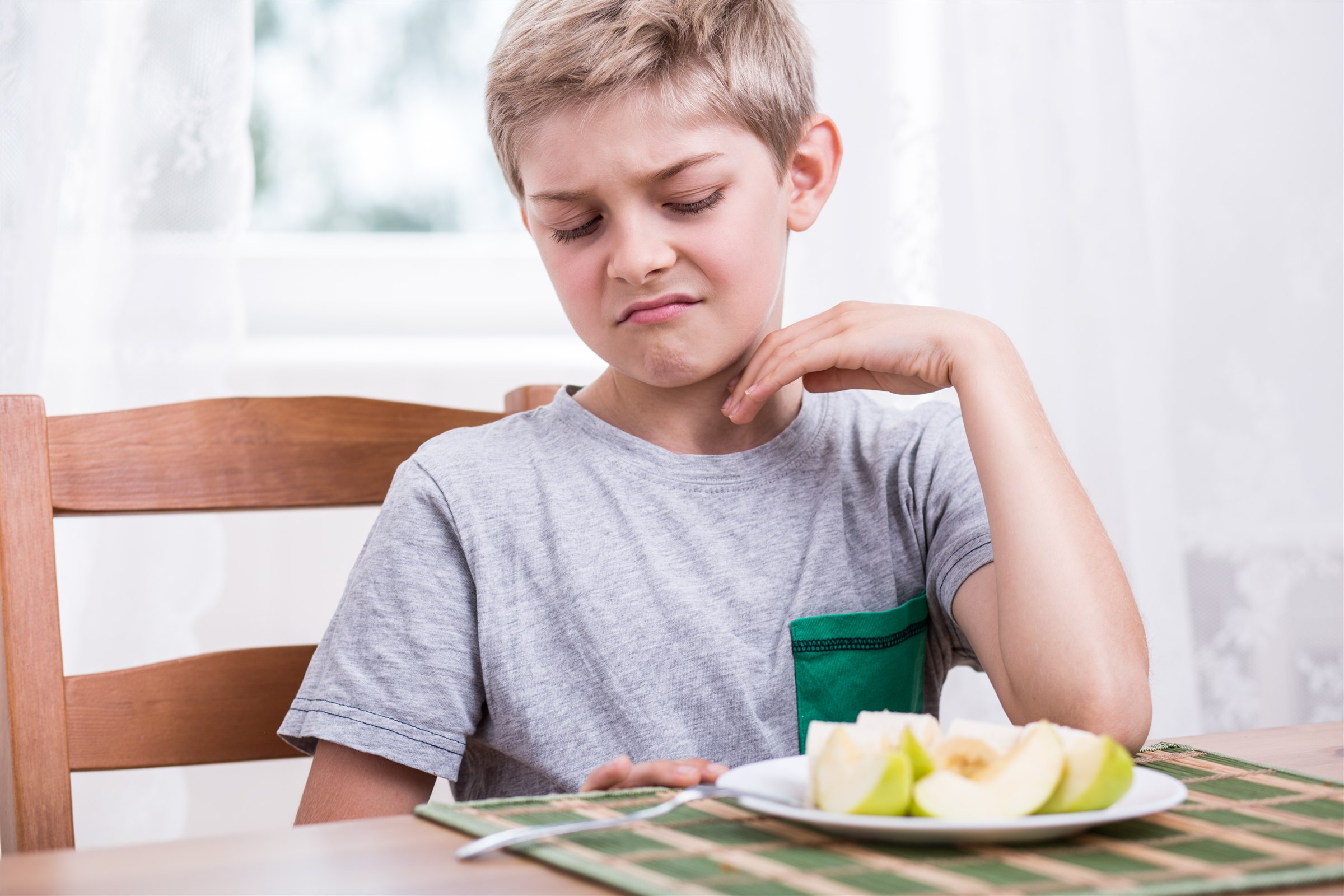 Child looking uncertain about a plate of sliced apples
